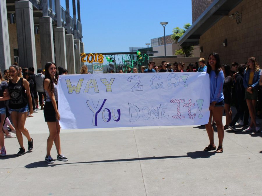 Juniors Olivia Mejia (left) and Tori Cudal (right) hold up a banner dedicated to the class of 2018 to show off as the seniors leave campus throughout the senior walk off.