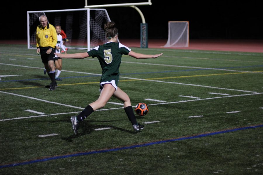As she kicks the ball up the side line, Mary Grace Feldman avoids the defending players. When she reaches the corner of the field, Feldman kicks the ball towards the goal where her teammates are ready to make a shot. 