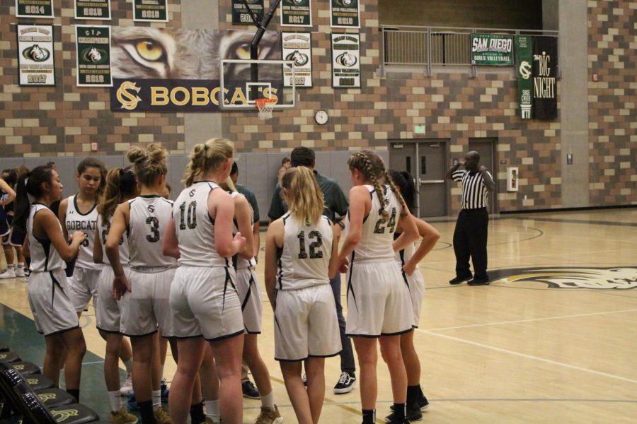 The varsity girls basketball team croud around coaches during a break in the game to discuss strategy. The girls resulted in losing 41-38 against Tri City High School, however, many of the girls believe this season to improve with the new leauge they will be competing against this year.