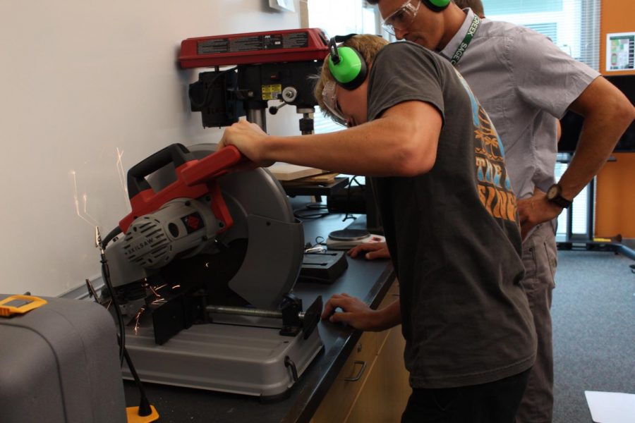 In Principles of Engineering class, Mr. Fieberg supervises Sophomore Peter Rubin operating on a saw machine, to cut a part for their project.