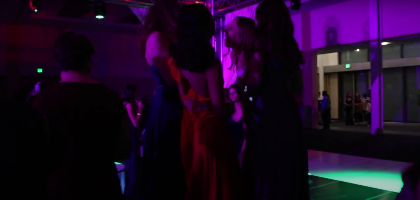 Four high school students talk and enjoy their time at a dance. The music was playing in the background while lights were shining everywhere.