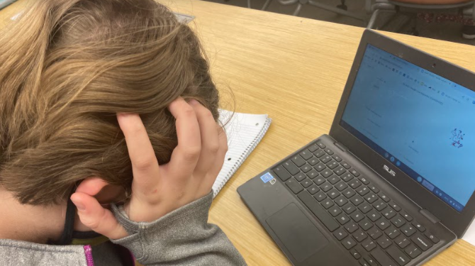 A stressed high school student rests her head in her hands. Contemplating college options while simultaneously managing schoolwork can be a lot of pressure for students.