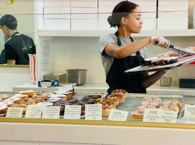 Pastry chef Alexis Wells places new doughnuts on the display rack for customers to buy. Every month, The Goods switch out their current doughnut flavors for new ones.