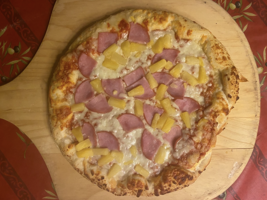 A Hawaiian pizza lays on a dining room table. This delicacy can be enjoyed in any form.