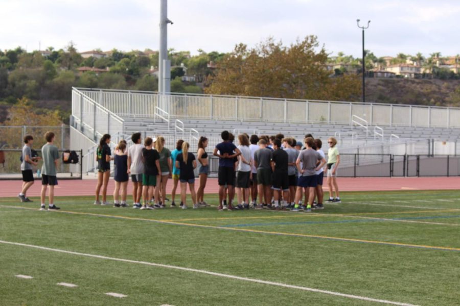 Cross Country teams huddle up before their practice recovery run. During the huddle, Coach Jason Jacobson tells his athletes the expectations for the practice ahead.