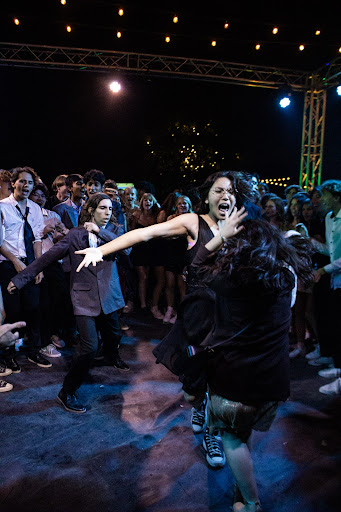 The crowd of party goers makes way for a dance circle. Three individuals in particular join in, representing the excitement of the night with their moves. 
