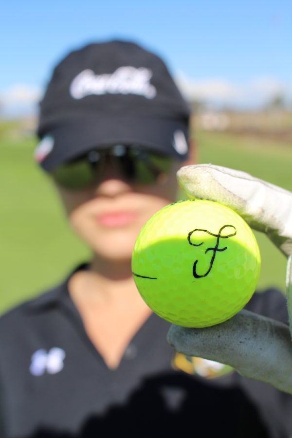 Fabi Sanchez holding up a golf ball with her first initial written on it.