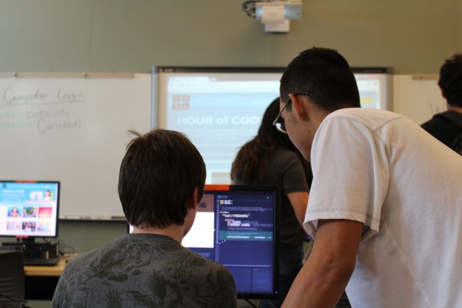 A fellow student helps another student how the coding process works during Hour Of Code, in the student library. 