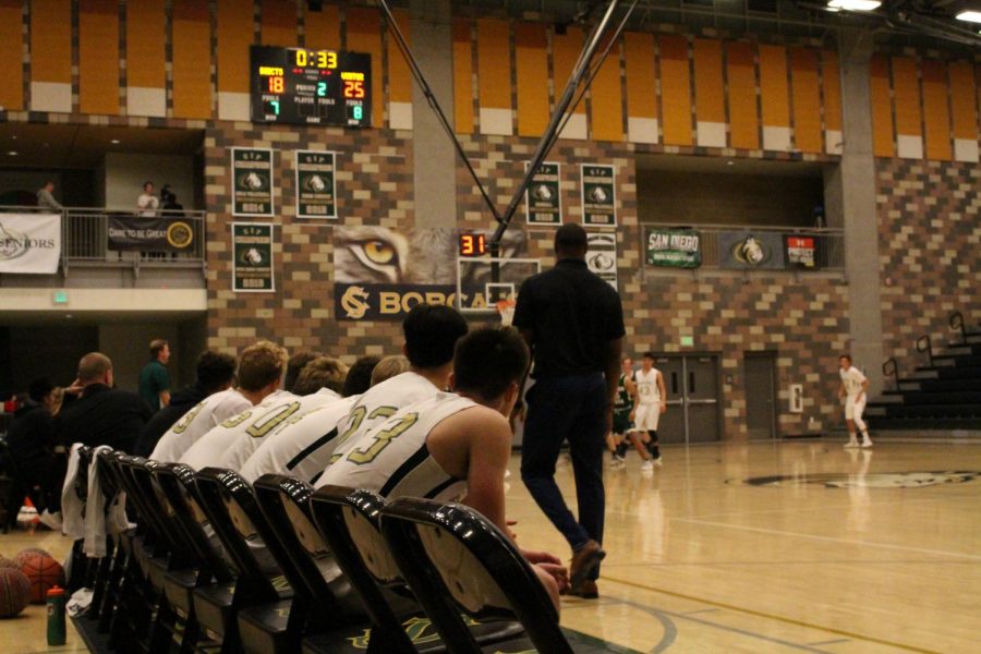 The boys varsity coach paces the sidelines as the score gets closer and closer. The team eagerly watches the game from the side waiting for their turn to go in and play. 
