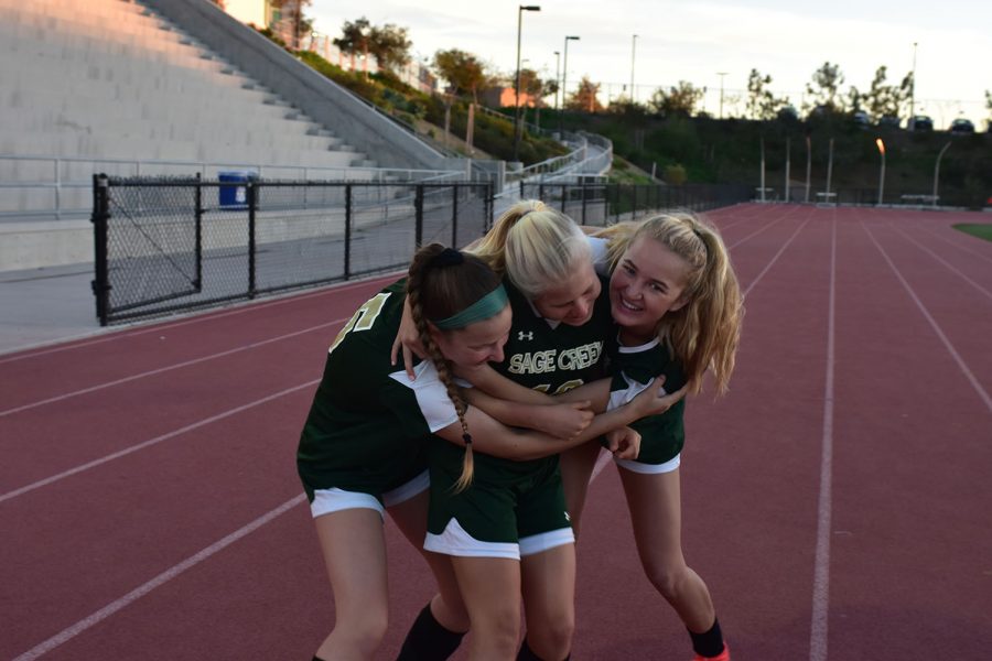 Varsity soccer players Mary Feldmann and Cierra Healy embrace Kat Sumwalt in a hug before preparing for their game last Tuesday, Nov. 27. The varsity team warmed up for their under the lights game while the junior varsity game was still taking place.