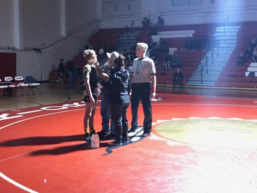 Freshman wrestler Peter Rubin gets his lip taped by Coach Brian Kirby as the referee and Fallbrook athletic trainer watch. On Thursday, Dec. 6, wrestling had a tri-duel against Fallbrook and Army Navy in which Rubin busted his lip. After the referee stopped the match two times due to the blood, Kirby decided to tape Rubin’s mouth closed in order to stop the blood. Rubin won both matches with a pin.