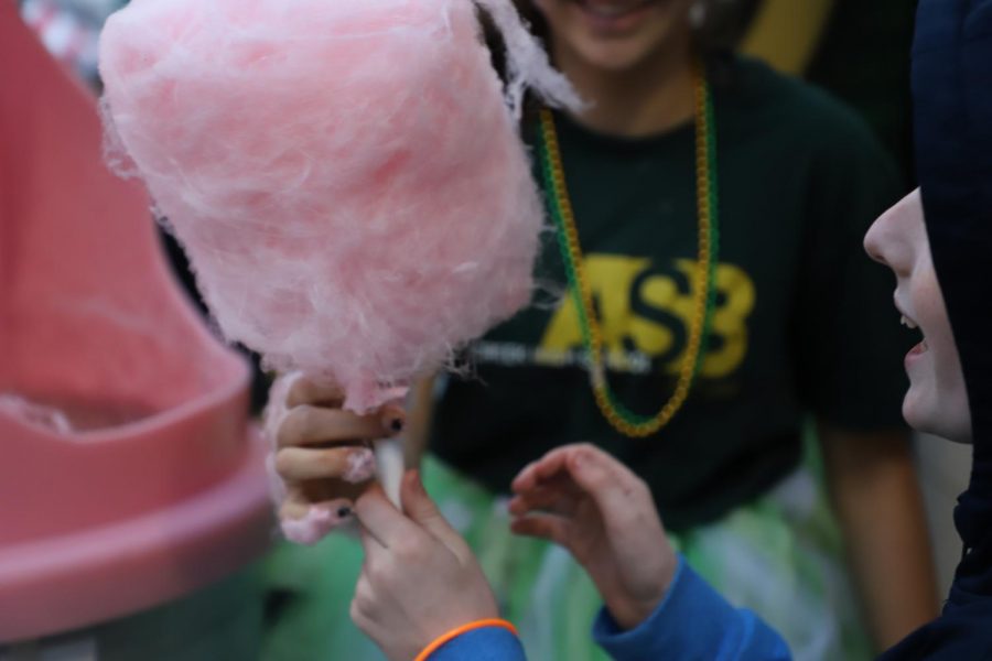 Freshman Zoebelle serves cotton candy to little kids before the start of the game. The athletic mall was filled with booths ranging in candy to games, to satisfy each students perfect idea of Hoopcoming.