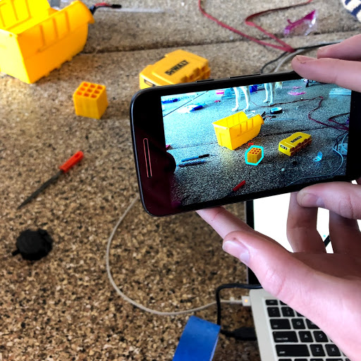 The hands behind the phone is junior Cole Savage, software lead of the Level Up team. He continues to update the most efficient way for their robot to locate the “waffle cubes” (a.k.a. yellow bricks). In order for their robot to know where it needs to go pick up the yellow bricks, the phone sends signals to it of where they are in relation to the field the robot is on and highlights what it needs to be picking up. 