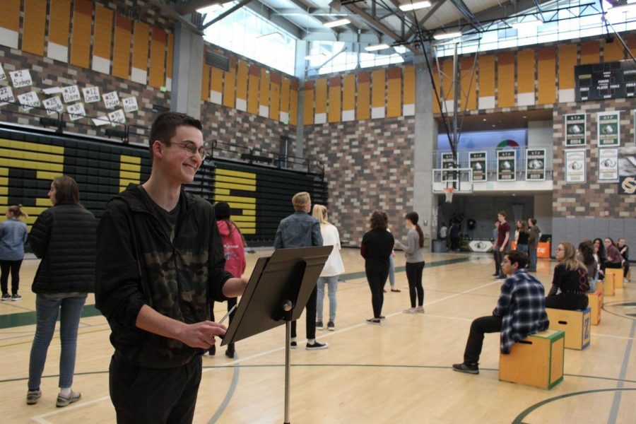 Junior Nicholas Tappin helps conduct the pit orchestra as the Matilda cast rehearses in the gym. They will be performing “Revolting Children” at the pep rally on Friday. 