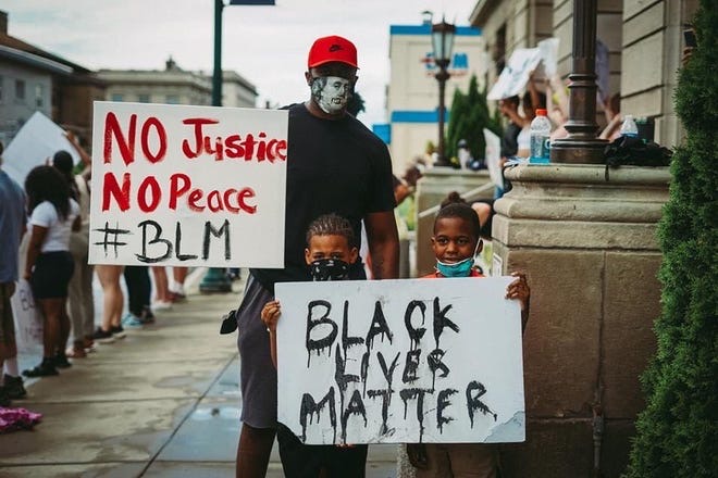 A father and his children stand with signs for the recent protests. The recent protests have been formed in hopes that Minnesota will prosecute the four officers involved with the death of George Floyd. 
