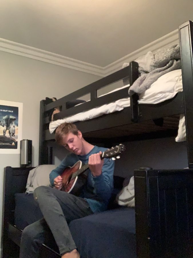 Freshman Blake Hafner practices on his guitar. Looking down at it and expressing his enjoyment for music. 