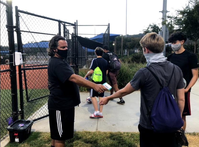 Assistant Coach Ray Ochoa uses a thermometer to measure a player’s temperature before allowing him to enter the field. Temperature checks and PPE are just some of the ways coaches have been trying to stay safe during practices.