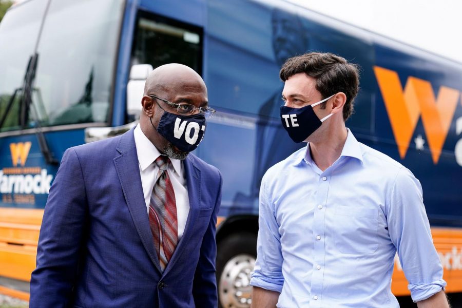 Ossoff and Warnock talk in front of a campaign bus. The two were both elected to the Senate on Jan. 6 and have given Democrats the majority in Congress.