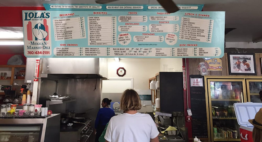  Lola’s 7 Up Mexican Market and Deli menu hangs from the ceiling with many of the delicious meals Lola’s has to offer customers. Behind the sign is Lola’s small kitchen, where the staff works hard to prepare the food.  