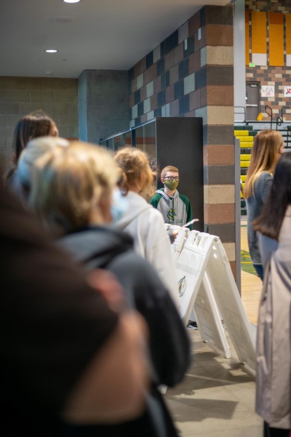 Eighth-graders listen attentively in the gym. The entrance of the gym has a trophy showcase in the front for all to see when walking in. 