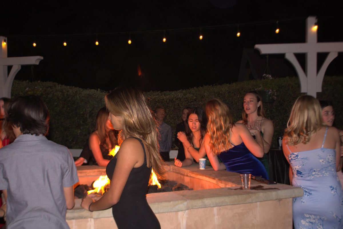 Students gather around the fire to escape from the evening chill. Drinks were served in near vicinity. 
