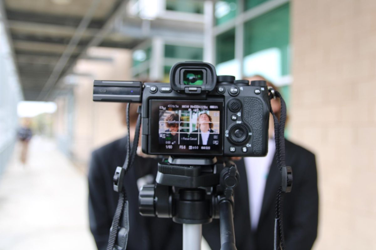 A Canon camera is posed towards two student journalists preparing to film. According to Pew Research Center, 9% of state capitol reporters in the US are student journalists. 