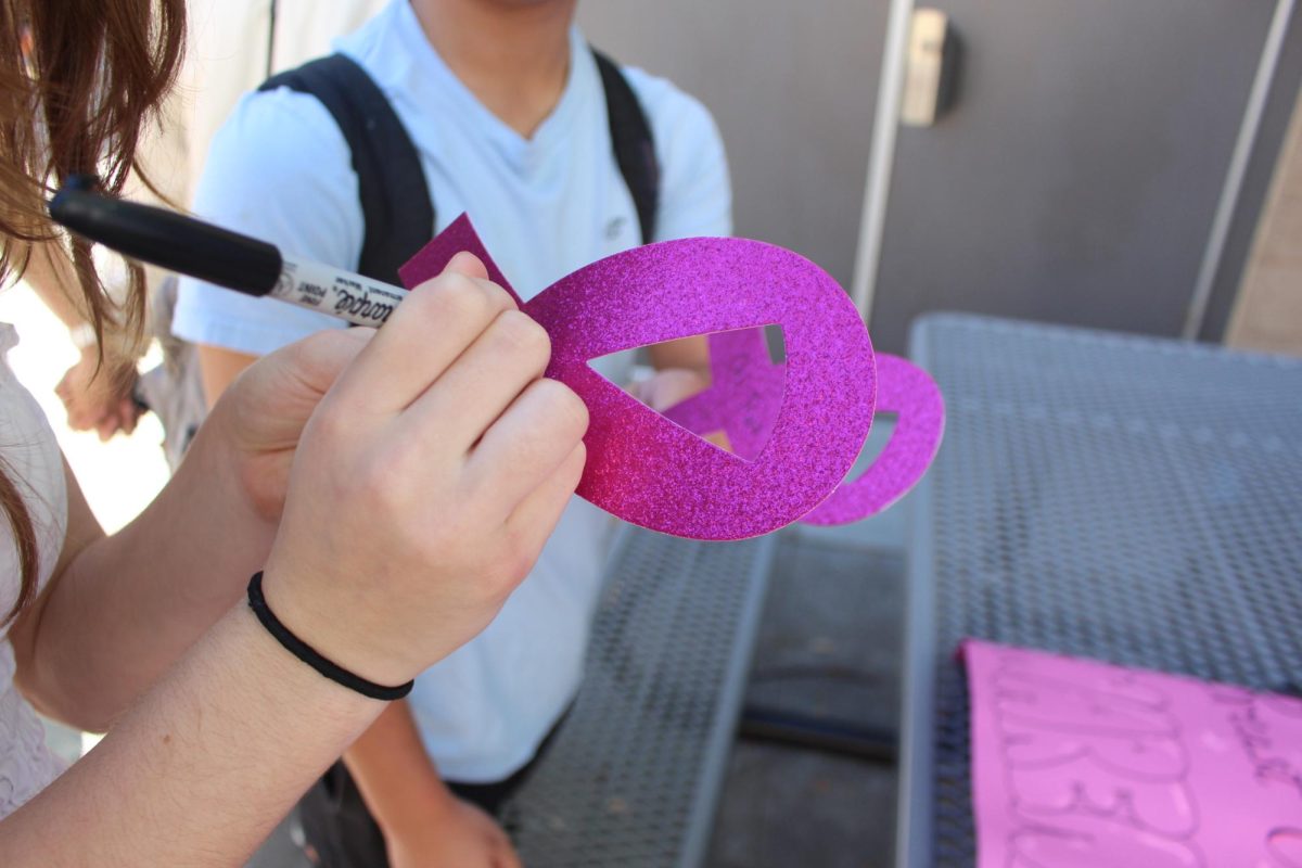 Two students are in the cutout writing their Pink Out Cards. These ribbons serve as a way to honor those who have fought or are fighting breast cancer.  