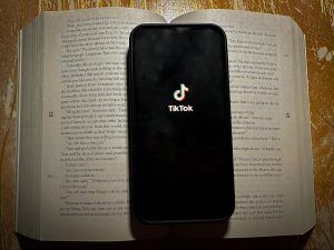 A TikTok loading screen is displayed on top of a book. It showcases the normalized prioritization of social media over knowledge.