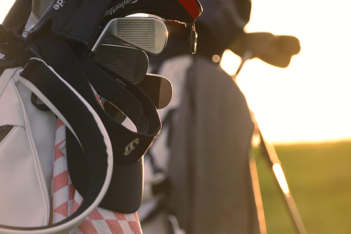 A Sage Creek visor hangs from a golf bag, against the warm glow of a Carlsbad sunset. The peaceful scene captures the quiet beauty of The Crossings golf course