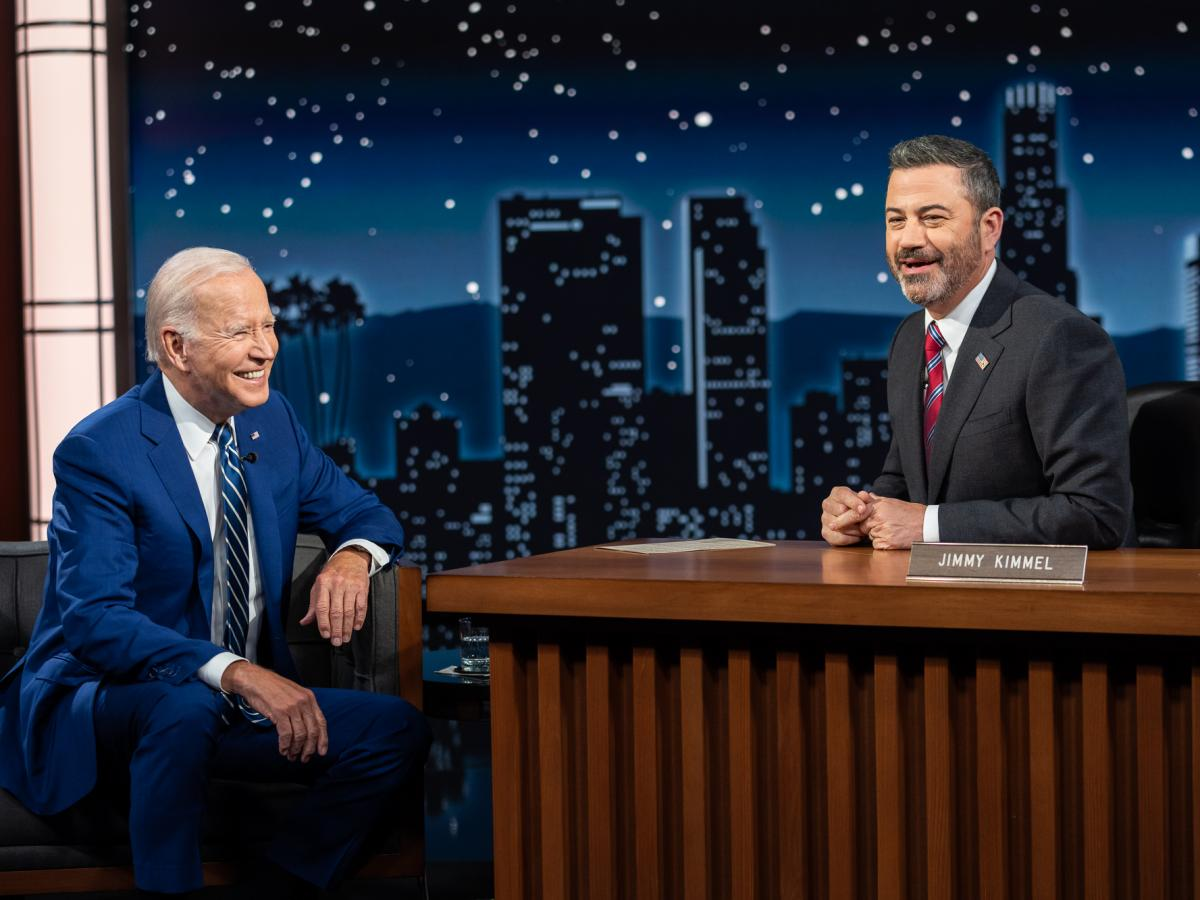 Jimmy Kimmel sits with President Biden. They are both laughing together.